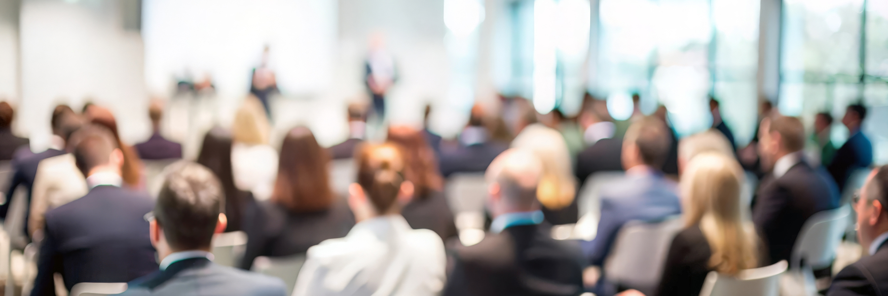A conference audience listens to a presentation on stage | Credit: Adobe Stock