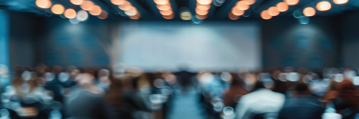 A conference audience listens to a presentation on stage | Credit: Adobe Stock