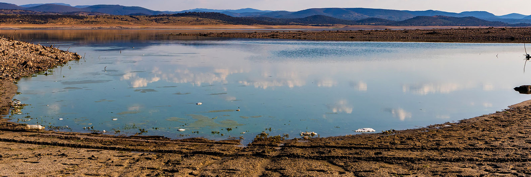 A western reservoir with low water levels and dry, cracked land surrounding with mountains in the background | Adobe Stock | Credit: Adobe Stock